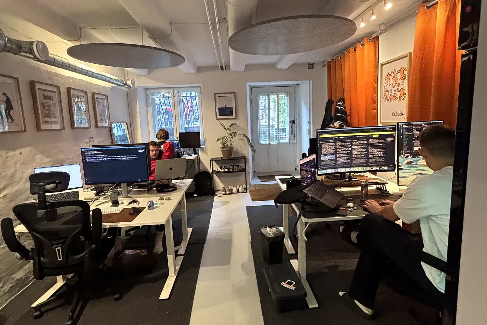 Et af lokalerne i Frederiksberg Co-working med medlemmer ved hæve-sænkeborde og orange gardiner